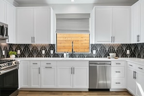 Cozinha moderna com armários brancos, lava-louças de aço inoxidável e painel de backsplash com padrão preto e branco.