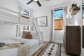 A room with a bunk bed, a desk, a chair, a window with curtains, a wooden cabinet, and a patterned rug. - East Austin 7BR | Shared Pool, Fire Pit & Yard (Austin)