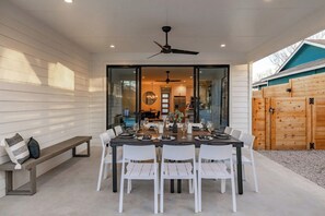 An outdoor dining area with a table set for six, surrounded by white chairs, and a ceiling fan above. - East Austin 7BR | Shared Pool, Fire Pit & Yard (Austin)
