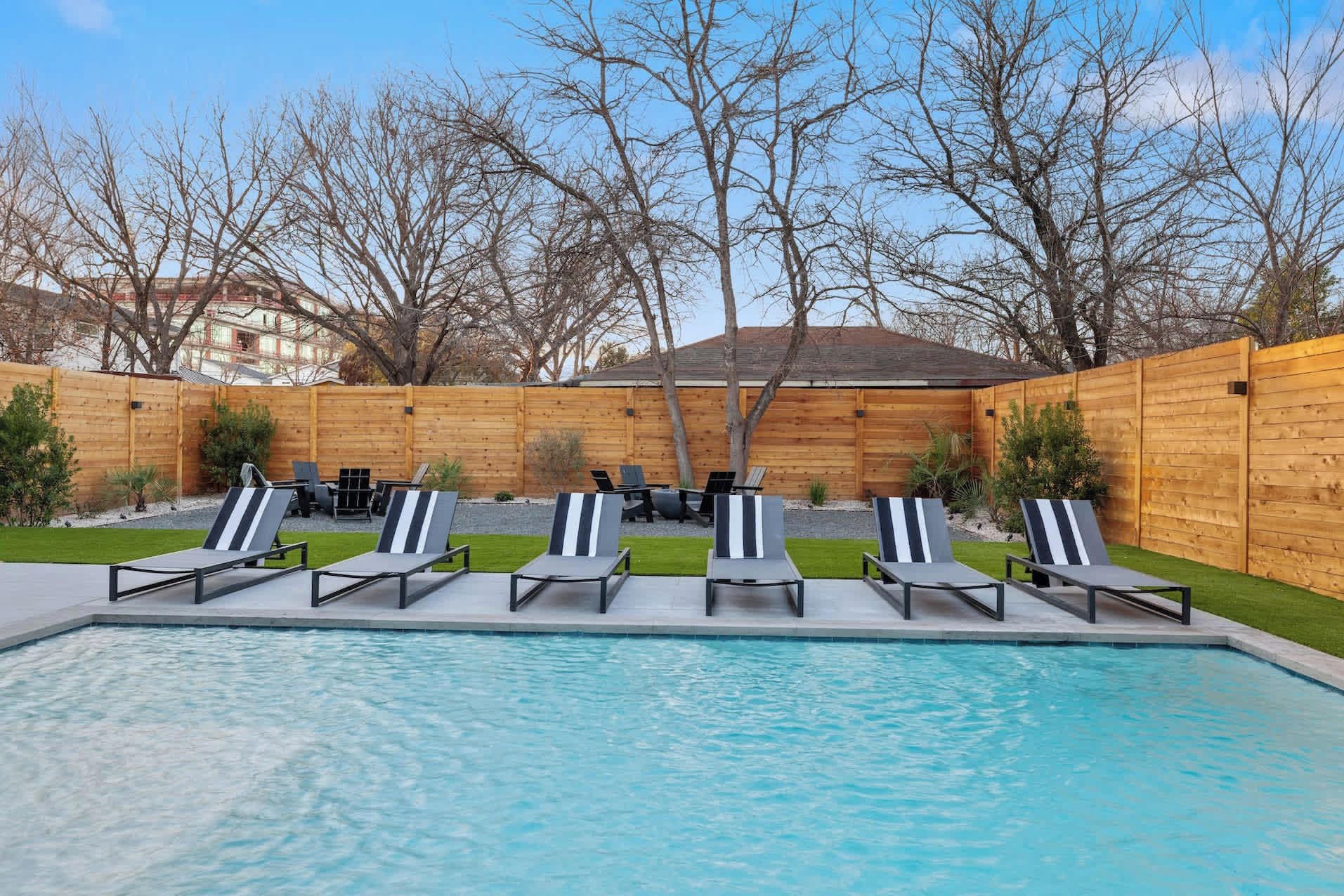 A swimming pool with lounge chairs and a wooden fence in the background.