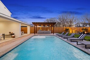 A backyard with a swimming pool, a bar area, and lounge chairs.