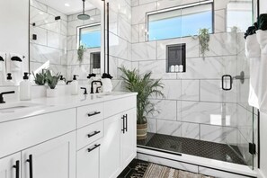 A modern bathroom with white marble tiles, a glass shower enclosure, and a large mirror.