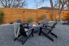 An outdoor seating area with a fire pit, four chairs, and a wooden fence in the background. - East Austin 7BR | Shared Pool, Fire Pit & Yard (Austin)