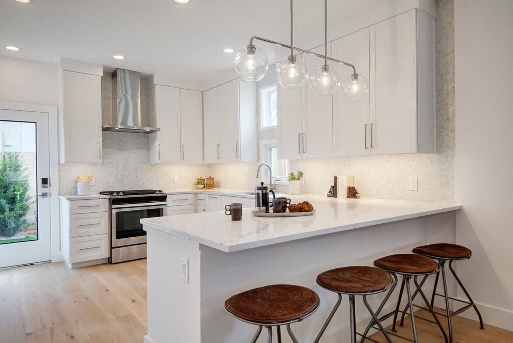 A modern kitchen with white cabinetry, a central island with stools, and pendant lighting.