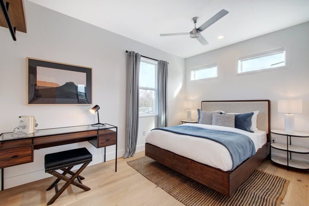 Een slaapkamer met een bed, bureau, stoel en een plafondventilator.