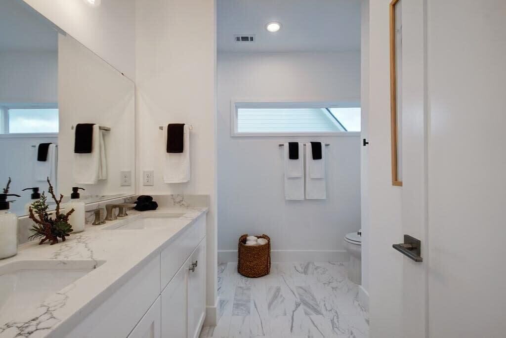 A modern bathroom with a white marble countertop, a large mirror, and a window above the sink.