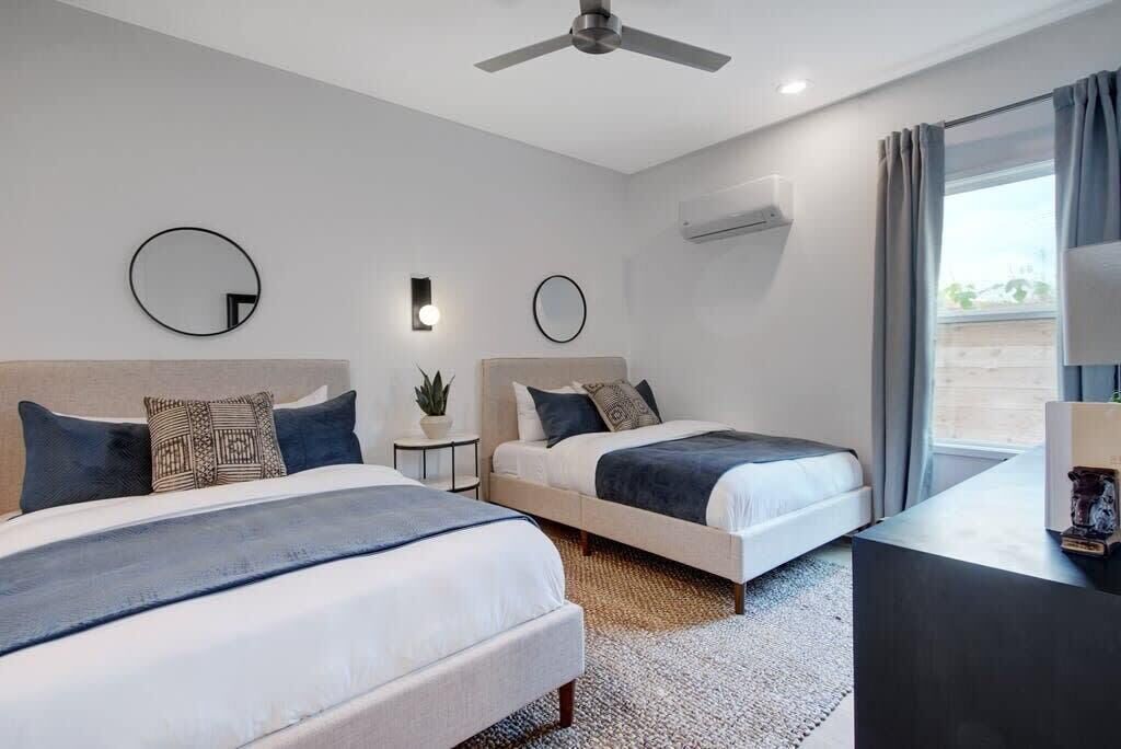 A hotel room with two beds, a ceiling fan, an air conditioning unit, and a view of the outdoors.