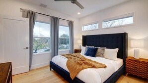 Une chambre moderne avec un grand lit, un ventilateur de plafond et deux fenêtres avec des rideaux.