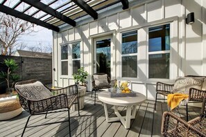 An outdoor patio with wicker furniture, a round table with fruit, and large windows. - Stylish 5BR Austin Home | Hot Tub & BBQ (Austin)