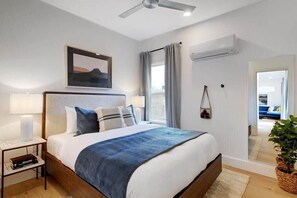 A bedroom with a bed, bedside table, lamp, and a view of the living area. - Modern Construction with Private Hot Tub (Austin)