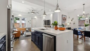 Une cuisine moderne dotée d’un îlot central, d’appareils électroménagers en acier inoxydable, de luminaires suspendus et d’un coin repas avec une table et des chaises.