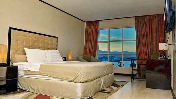 Habitación de hotel con una cama grande, un escritorio, un televisor y una ventana con vistas a la ciudad.