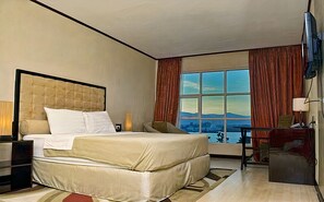 Ein Hotelzimmer mit einem großen Bett, einem Schreibtisch, einem Fernseher und einem Fenster mit Blick auf die Stadt.