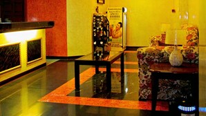 Un hall de hotel con una mesa de recepción, una zona de estar con un sofá floral y un jarrón decorativo sobre una mesa.