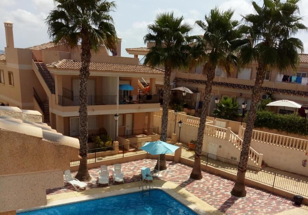 Un área de piscina con sillas de descanso, palmeras y un edificio con balcones.