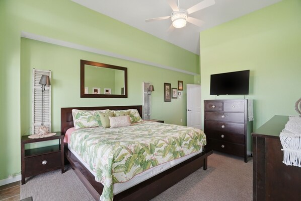 Une chambre à coucher comprenant un lit, des tables de chevet, une commode, un téléviseur et un ventilateur de plafond.
