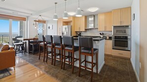 Een moderne keuken met een centraal eiland, barkrukken, roestvrijstalen apparatuur en houten kastjes.