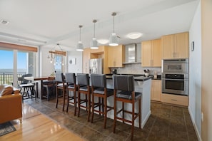 A modern kitchen with a central island, bar stools, stainless steel appliances, and wooden cabinets.