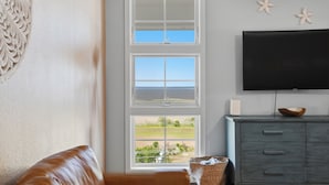 Een woonkamer met een groot raam, een flatscreentelevisie, een grijze kast en een rieten mand.