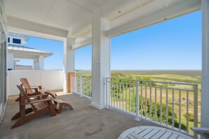 A covered balcony with a view of the landscape, a wooden table, and two Adirondack chairs.