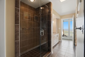 A modern bathroom with a glass-enclosed shower, tiled walls, and a view of a balcony.