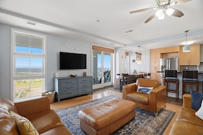 A spacious living room with a large TV, leather sofas, and a view of the outdoors.