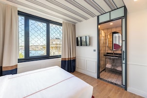 Habitación de hotel con una cama grande, un televisor montado en la pared, un baño con espejo y lavamanos, y vistas a través de una ventana con cortinas.