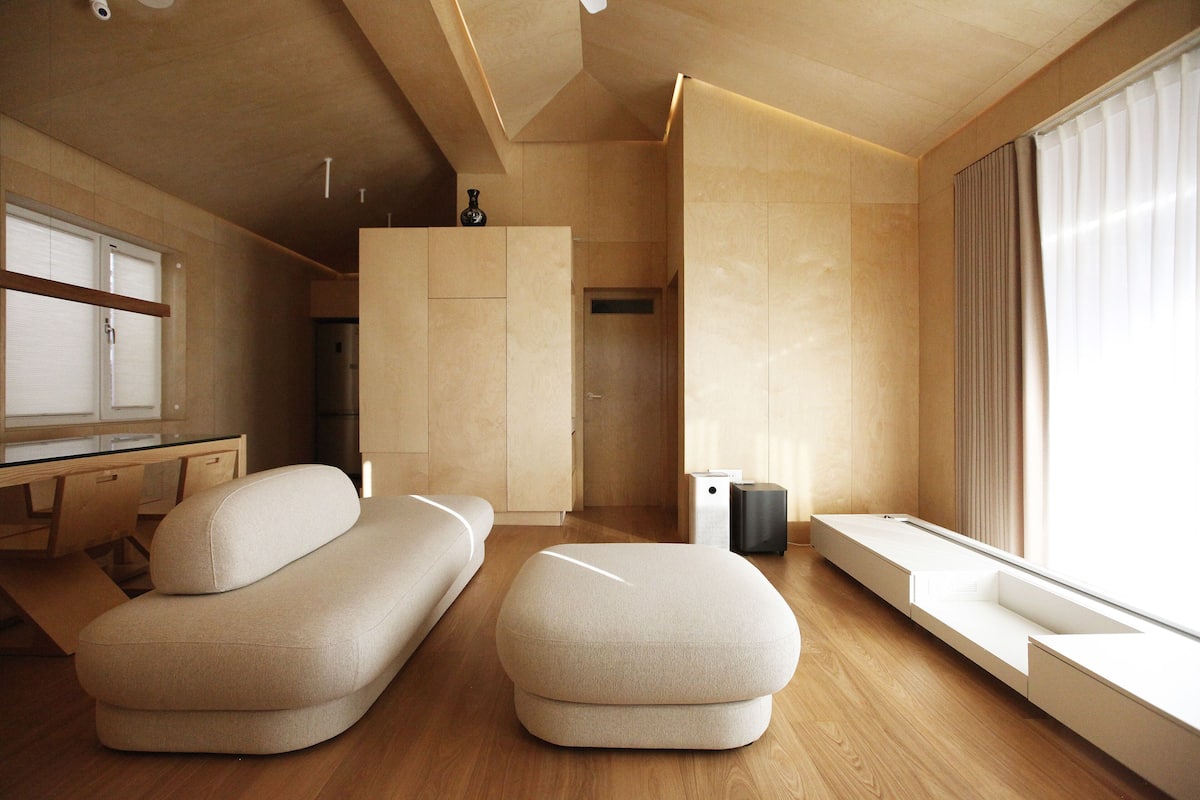 A modern, minimalist room with a wooden floor, a sofa, a bench, and a window with curtains.