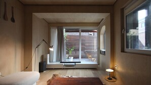 A modern living room with a sofa, a wooden bench, a floor lamp, and a view through a sliding glass door to an outdoor area with a plant and a chair. - Homegarden Park (Pyeongtaek)