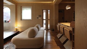A modern living room with a sofa, wooden flooring, a ceiling fan, and a kitchen area with a countertop and cabinets. - Homegarden Park (Pyeongtaek)