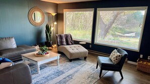 Een moderne woonkamer met een grijze bank, een witte salontafel, een beige fauteuil en een blauw gestreept vloerkleed.