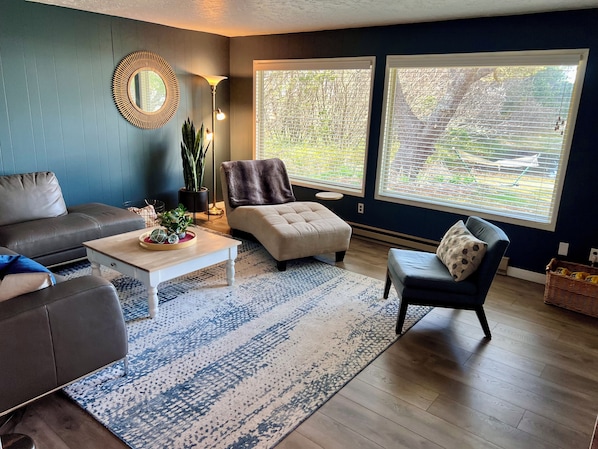 A modern living room with a grey sofa, a white coffee table, a beige armchair, and a blue patterned rug.