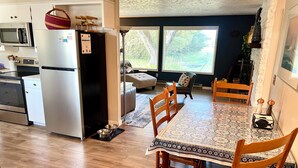 Een moderne keuken met roestvrijstalen apparatuur, een eethoek met een tafelkleed met dessin, en een uitzicht op de omgeving door grote ramen.