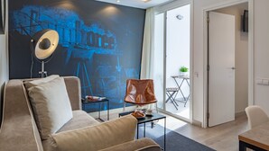 Ein modernes Wohnzimmer mit einer Couch, einem Couchtisch und einem Ledersessel. Ein großes Fenster bietet Blick ins Freie.
