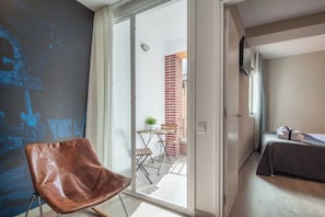 A hotel room with a sliding glass door leading to an outdoor area, a bed with a grey bedspread, and a brown leather chair.