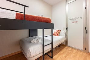 Une chambre avec des lits superposés, une porte sur laquelle est inscrit « JAZZ BCN HOT » et un mur blanc.