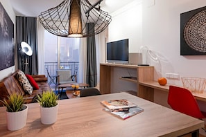 Una sala de estar moderna con una mesa de comedor, sofá y televisor. Hay plantas en macetas sobre la mesa y una silla roja.