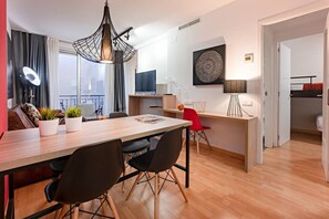 Un salon moderne avec une table à manger en bois, des chaises noires, un fauteuil rouge, un luminaire suspendu, un téléviseur et un élément décoratif mural.