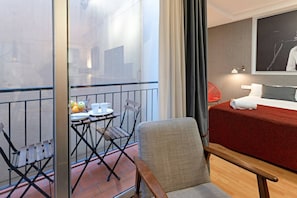 Une chambre d’hôtel avec un lit, une petite table sur laquelle se trouvent des fruits et des tasses, une chaise et un balcon doté d’une balustrade.