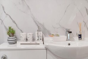 A bathroom with a white marble sink, a potted plant, and a few toiletries on the counter.