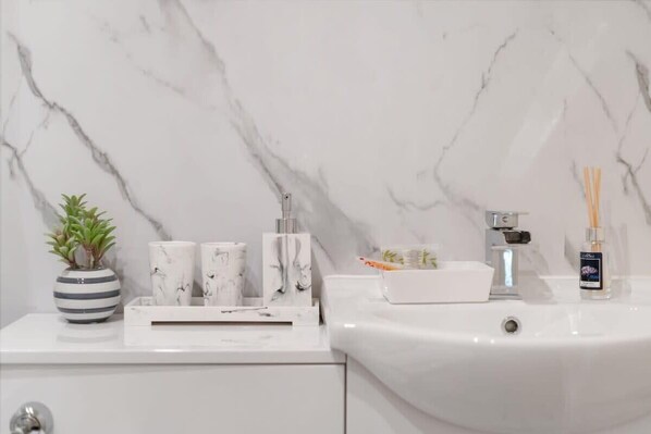 A bathroom with a white marble sink, a potted plant, and a few toiletries on the counter.
