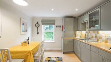 A compact kitchen with a dining area, featuring a yellow tablecloth, white chairs, and a patterned rug.