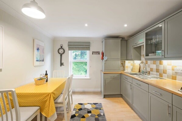 Une cuisine compacte avec un coin repas, agrémentée d’une nappe jaune, de chaises blanches et d’un tapis à motifs.