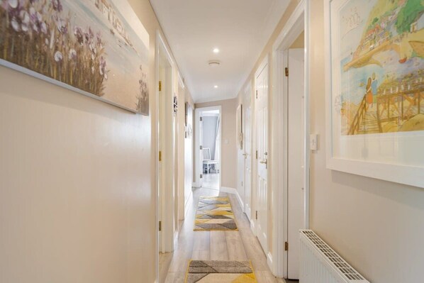 A hallway with a patterned rug, framed artwork on the walls, and a radiator on the floor. - Stylish Apartment with Private Parking, Torquay (Torquay)