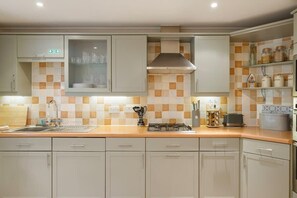 Een keuken met lichte kastjes, een betegelde spatwand, een fornuis en diverse keukengerei.