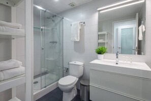 A modern bathroom with a glass-enclosed shower, a toilet, a sink with a mirror, and a small potted plant.