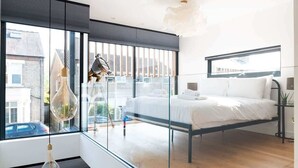A modern bedroom with a bed, a hanging light fixture, and a view of the street through large windows. - Stylish Cambridge 1-bed Home with free parking (Cambridge)