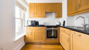 A modern kitchen with wooden cabinets, a stainless steel oven, and a black countertop. - Calm Leicester Sq 1BR (London)
