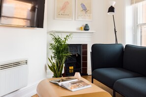 A living room with a fireplace, a sofa, a floor lamp, and a magazine on a table. - Calm Leicester Sq 1BR (London)