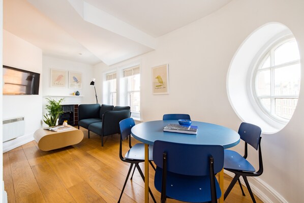 A modern living room with a round blue table, black chairs, a blue sofa, and a fireplace. - Calm Leicester Sq 1BR (London)